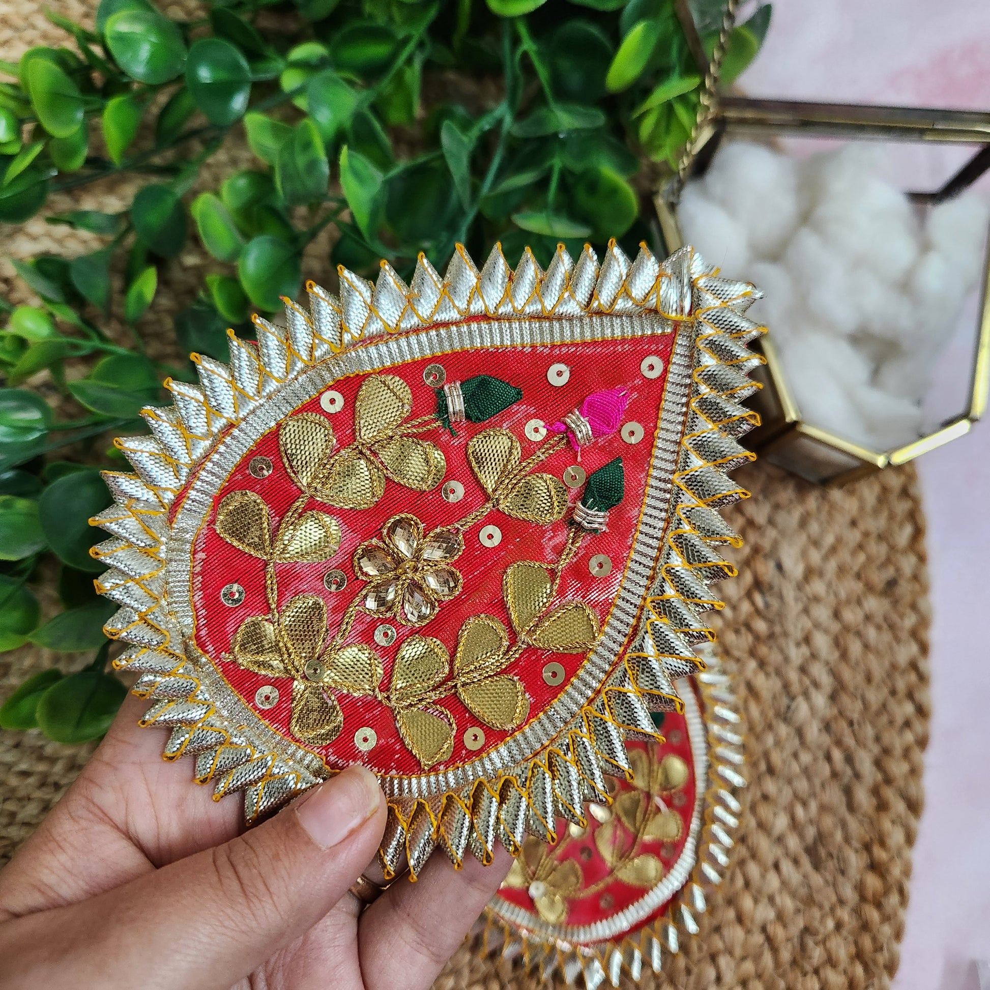 Decorative red and gold embroidered panel held by a hand with a natural background
